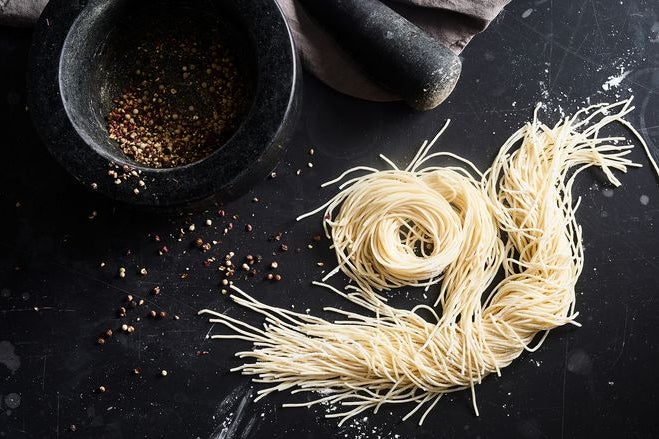 A small bowl of topping sits on a black table next to pasta twisted into spirals.